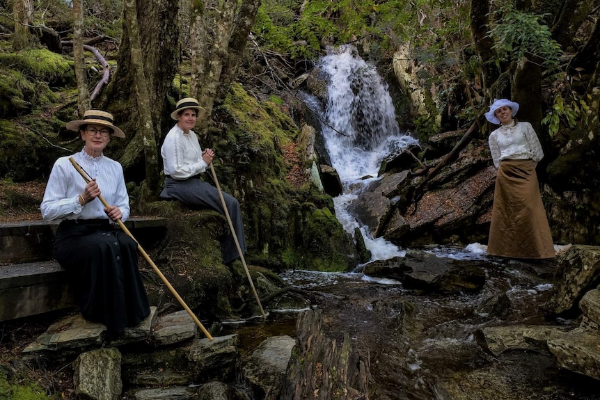 Three women in Edwardian dress posing by a waterfall.