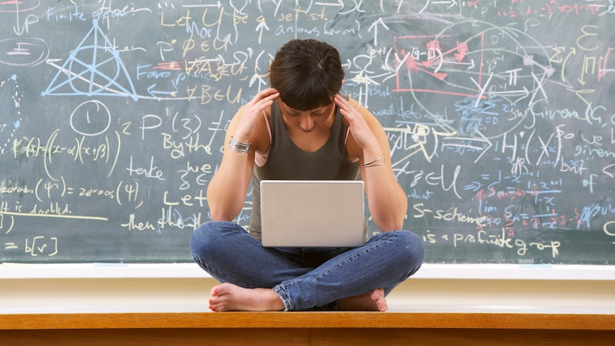 Woman sitting crosslegged with laptop in front of blackboard