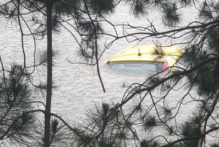 A yellow car is completely underwater except for the top of its roof.