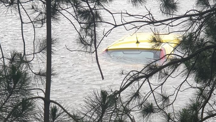 A yellow car submerged in a dam with trees framing the image.