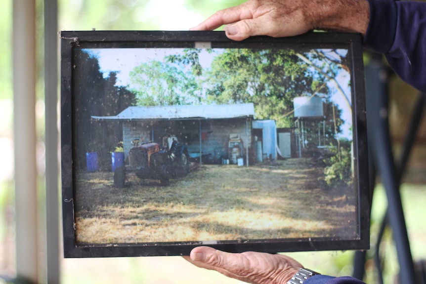 A man's hands hold a photograph of a house