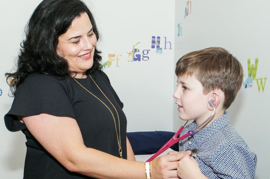 Dr Maria Boulton treats a child patient, holding a stethoscope to the boy's chest.