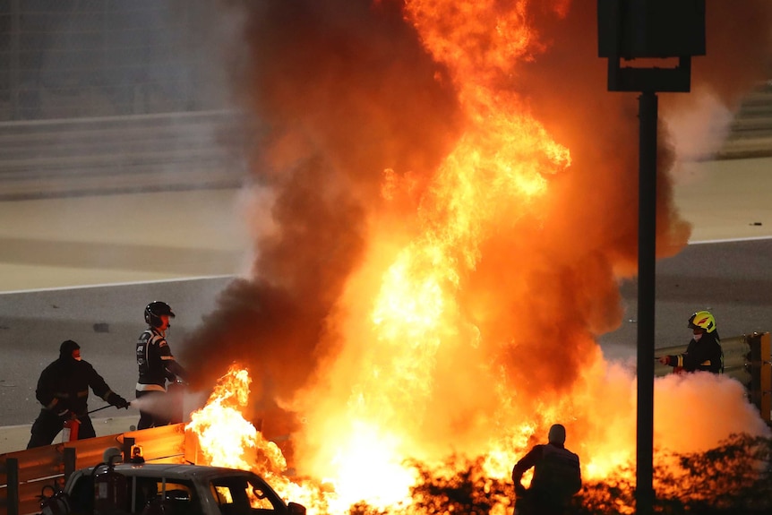 Volunteers try to put out a big fire that is consuming a Formula One car at the side of a track.