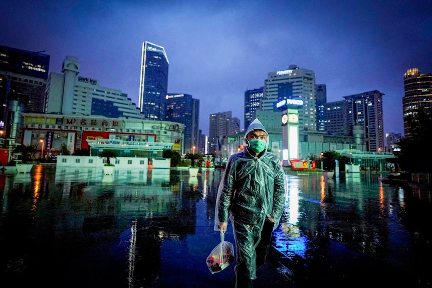 A man in a blue face mask and raincoat walks through Shanghai's streets during an evening rainstorm