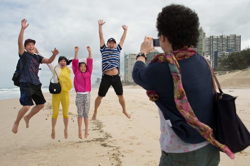 A group of Chinese tourists jump as a photo is taken on a Gold Coast beach