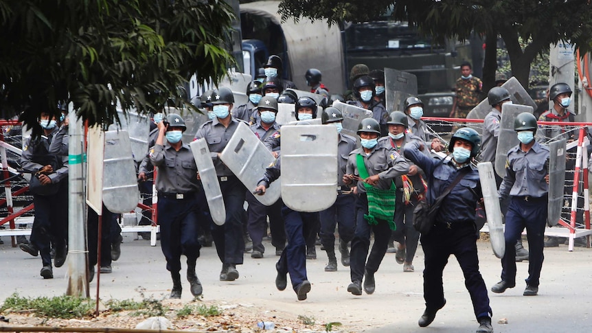 Riot police with shields charge towards a crowd of protesters.