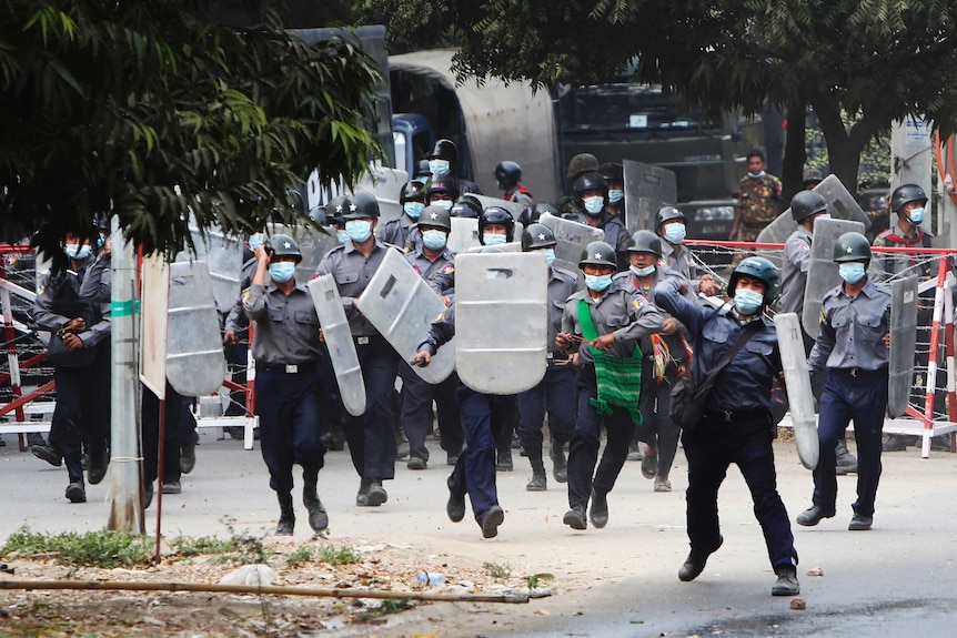 Riot police with shields charge towards a crowd of protesters.