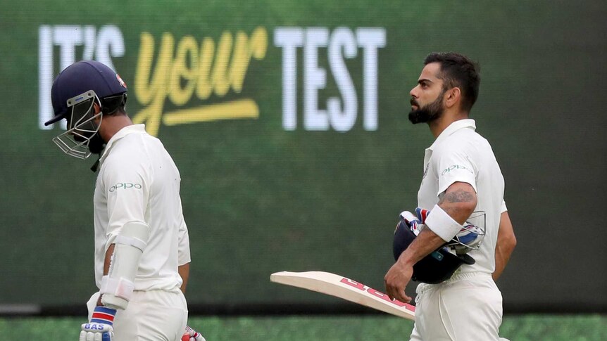 Indian batsmen Virat Kohli and Ajinkya Rahane walk together while a sign says "It's your Test" in the background.