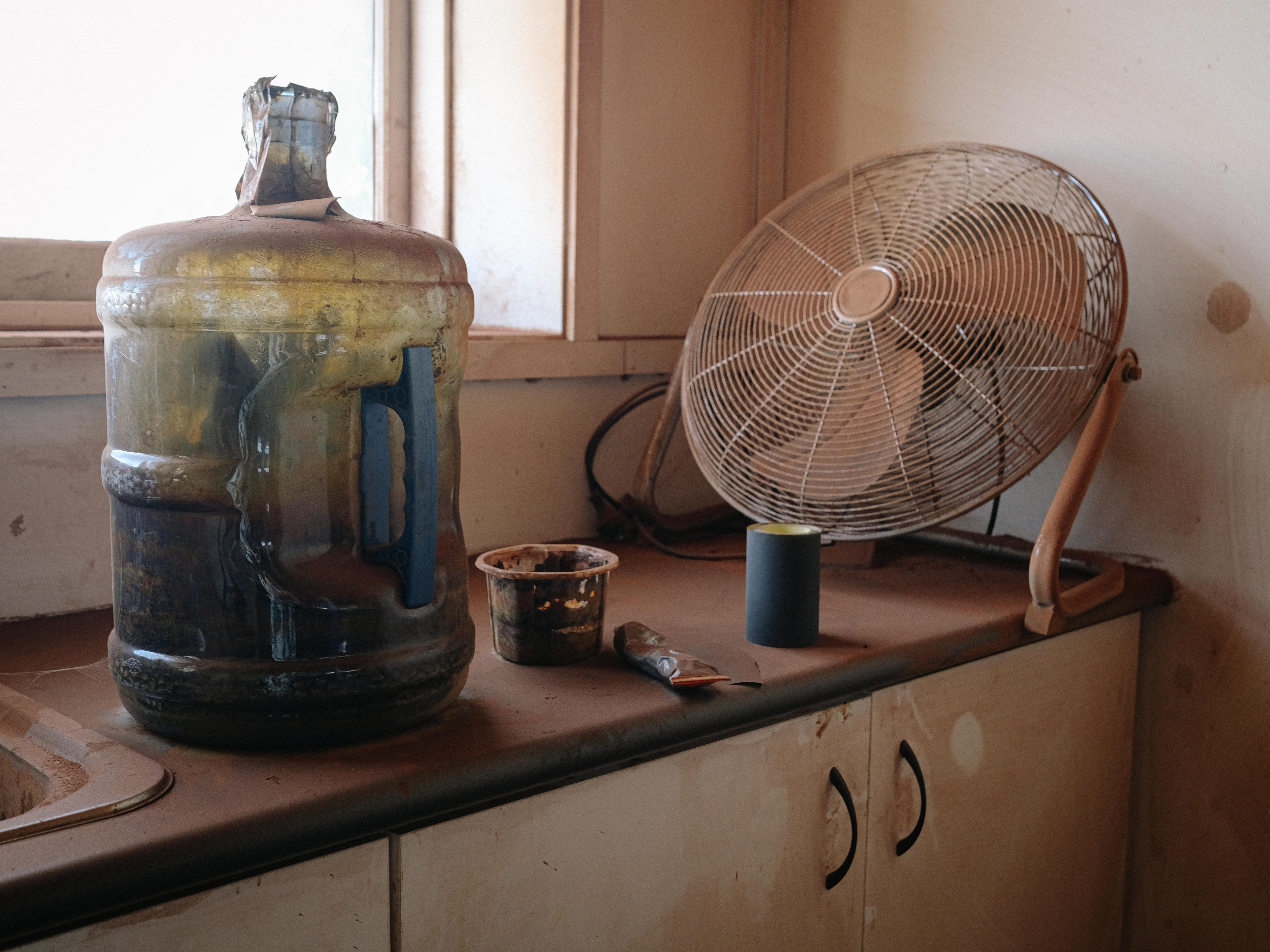 A waterbottle and fan sit covered in red wood dust on a bench in the studio