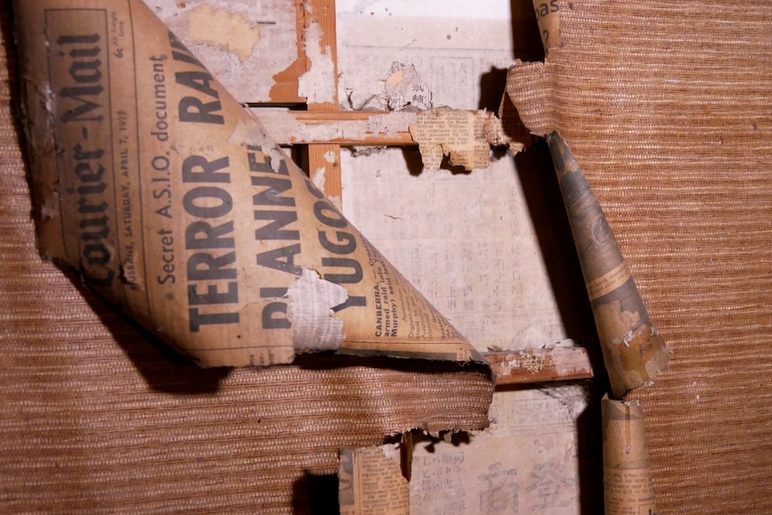 A wall lined with ripped newspaper and paper with Japanese characters