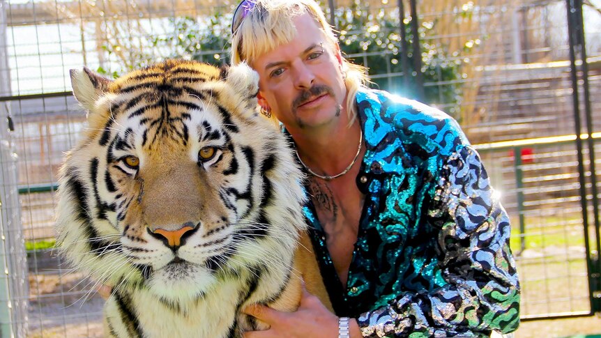A picture of a blond man with a moustache and sparkly top with a tiger.