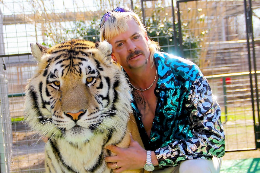 A picture of a blond man with a moustache and sparkly top with a tiger.