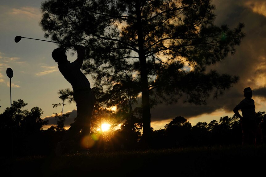 A golfer is seen in silhouette as he takes his tee shot in the fading light at the Masters.