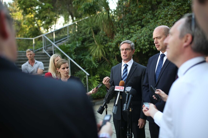 A wide shot showing Mike Nahan talking alongside Dean Nalder to a group of journalists in the WA Parliament fern garden.