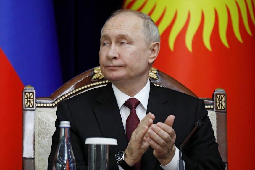 Vladimir Putin claps his hands as he looks over his shoulder.