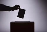 An unidentified person places a ballot into a box.