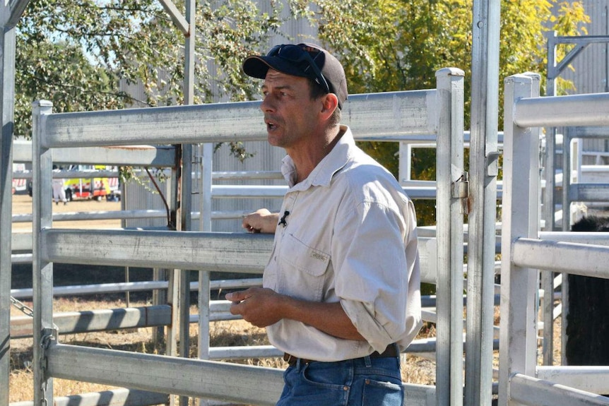 Man in front of metal gate in a rural setting.