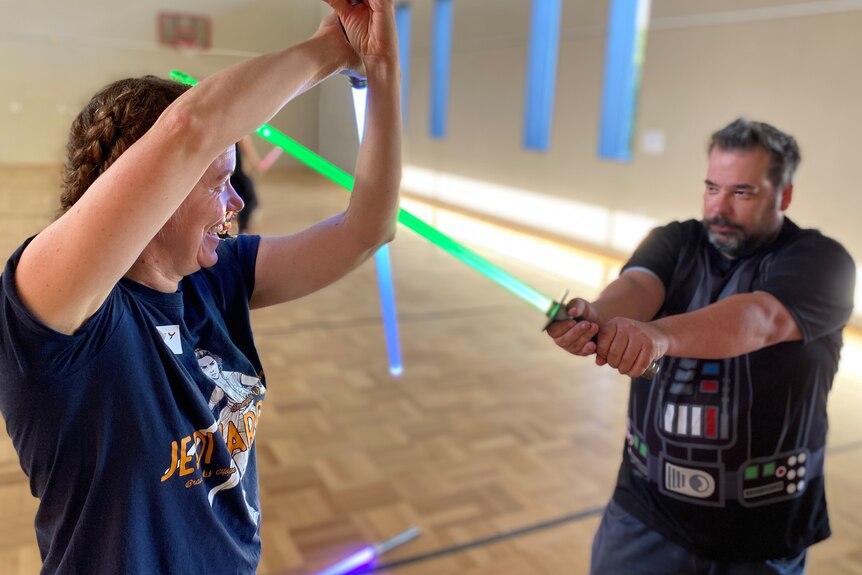 A woman wielding a toy lightsabers blocks an attack by a man