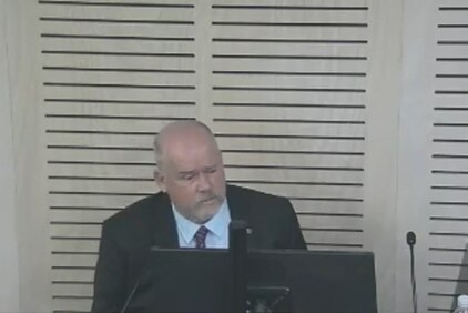 Bald man with beard in navy suit and white shirt sitting behind a desk