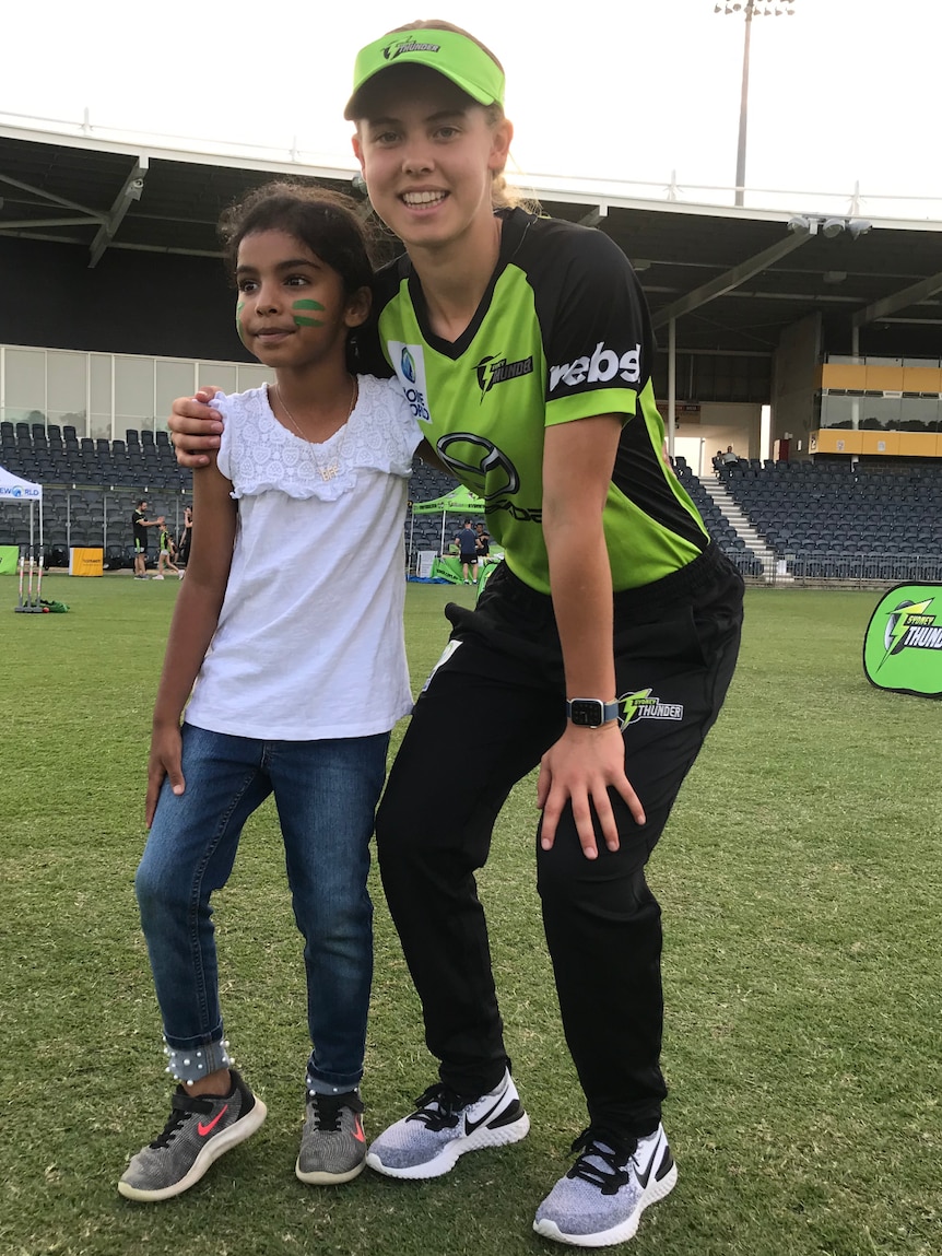 A Sydney Thunder WBBL player kneels as she poses for a photograph with a young supporter.