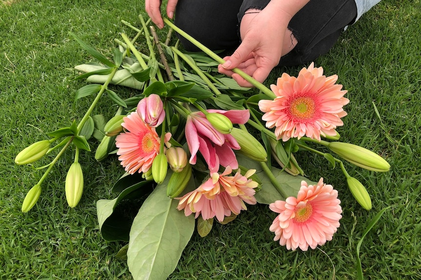 A bunch of pink and orange flowers lying on grass.