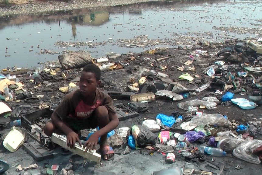 Boy crouches amongst e-waste at Agbogbloshie dump in Ghana.
