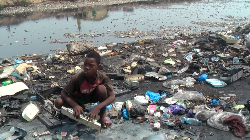 Boy crouches amongst e-waste at Agbogbloshie dump in Ghana.
