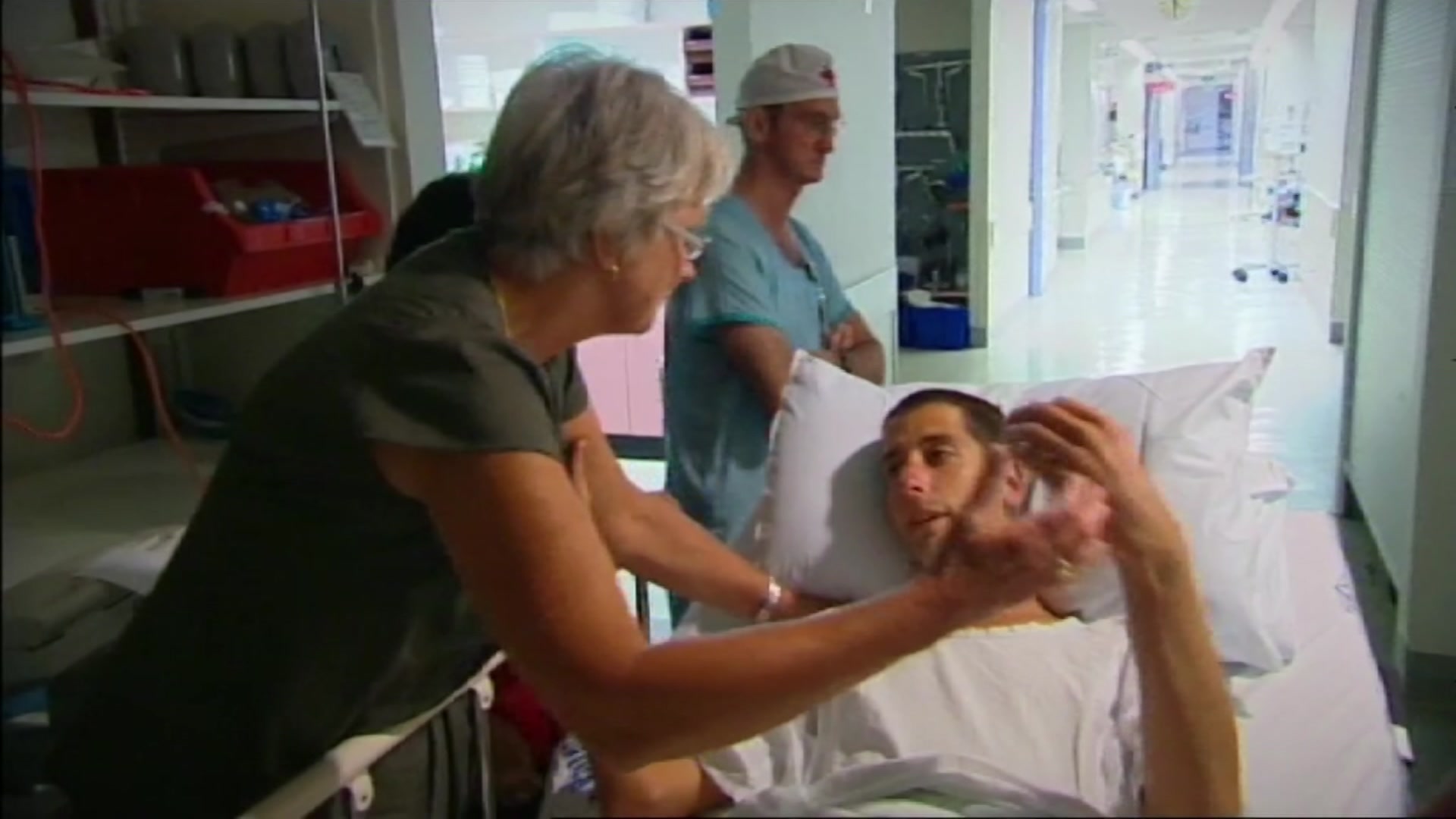 A man in a hospital bed preparing to hug a woman.