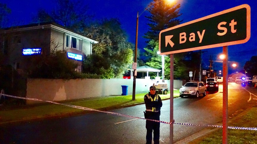 A policeman stands outside serviced apartments and a sign pointing to Bay Street in Brighton.