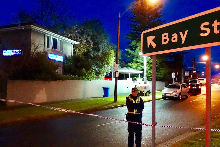 A policeman stands outside serviced apartments and a sign pointing to Bay Street in Brighton.