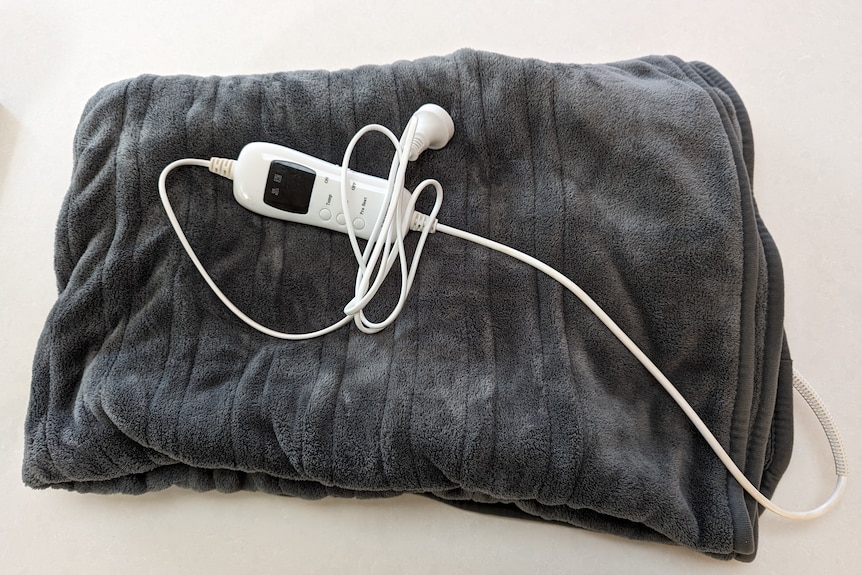 A fluffy grey heated throw blanket is folded on a white surface, with the power cord gathered on top.