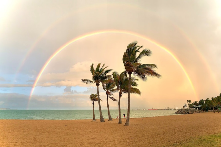 A double rainbow stretches over the sand and palm trees at the beach known as The Strand in Townsville.