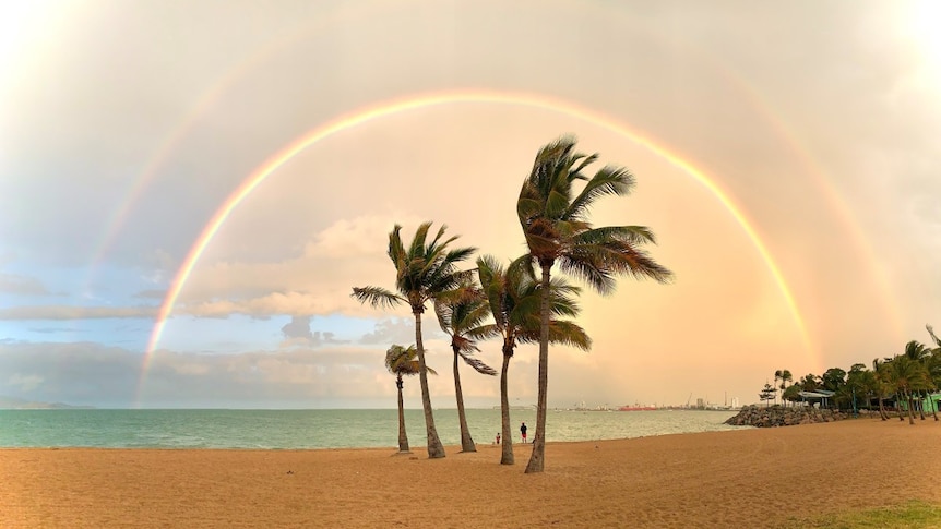 A double rainbow stretches over the sand and palm trees at the beach known as The Strand in Townsville.