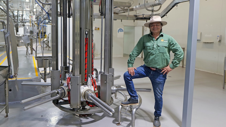 A man stands near some equipment. He is smiling, wearing a broad brim hat with a superman belt buckle