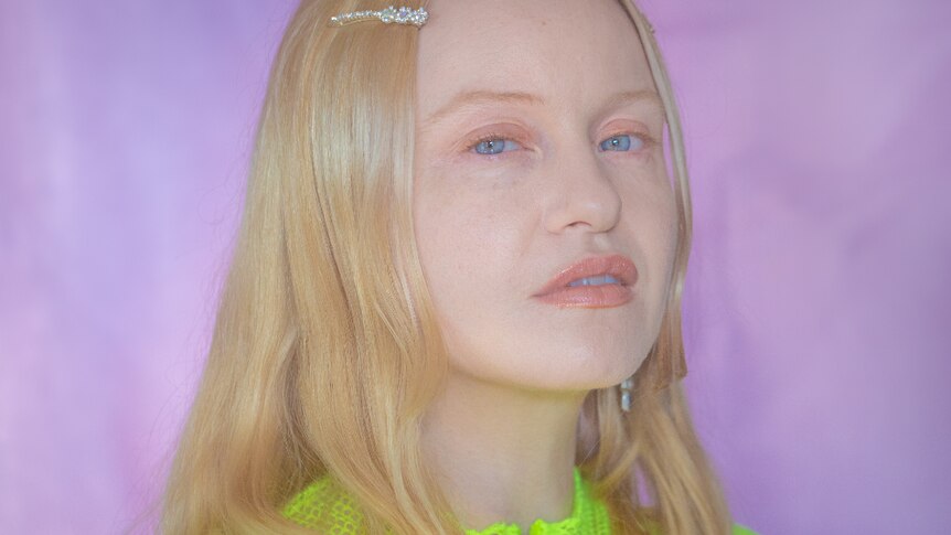 Press shot of KUČKA, wearing neon green shirt, against purple background