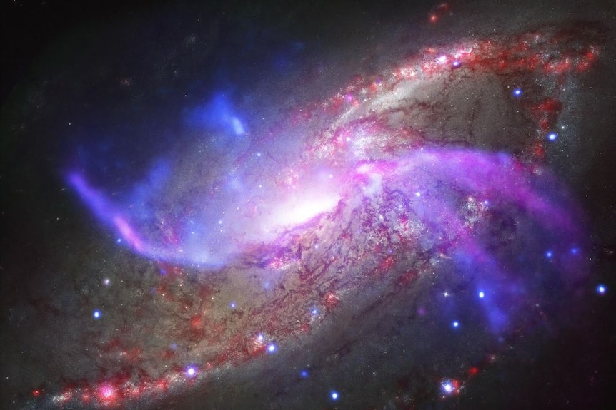 A beautiful spiral galaxy with a supermassive black hole at it's centre, shown in reds and blues and browns.