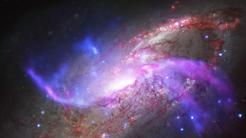 A beautiful spiral galaxy with a supermassive black hole at it's centre, shown in reds and blues and browns.
