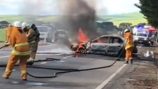 Firefighters with hoses near a flaming car