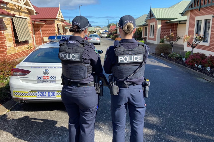 Two female police officers stand near a police car and retirement village