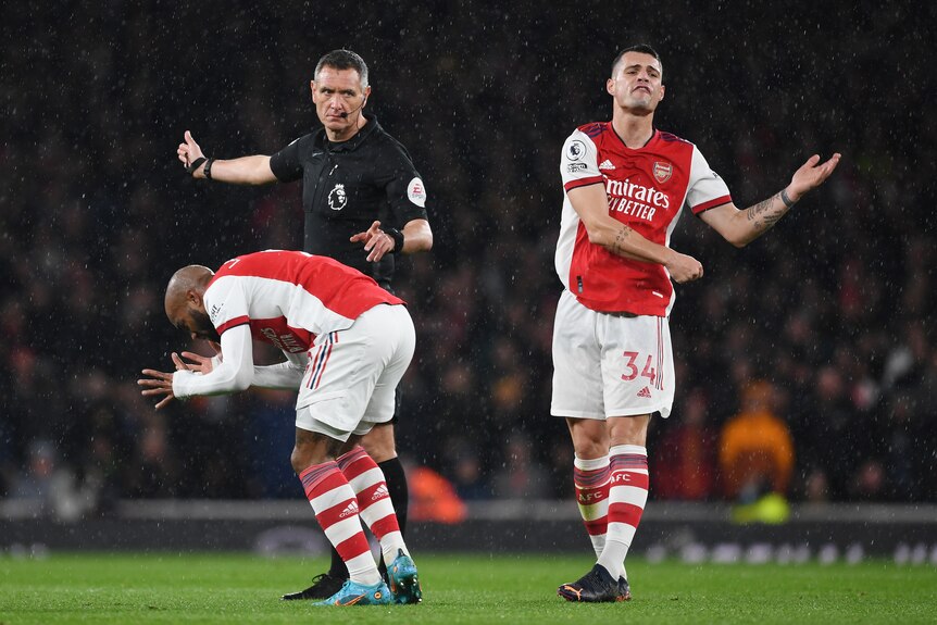 Alex Lacazette bends over and Granit Xhaka appears to say something as a referee holds out his hand behind them 