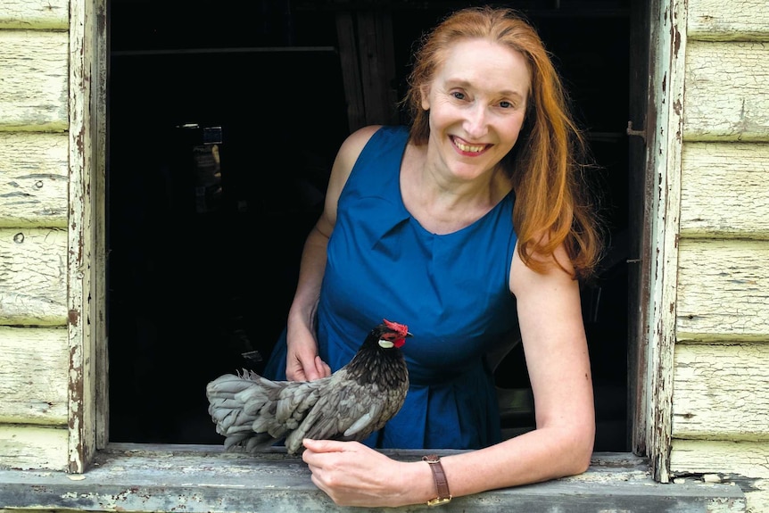 A woman poses in a window frame with a small chicken