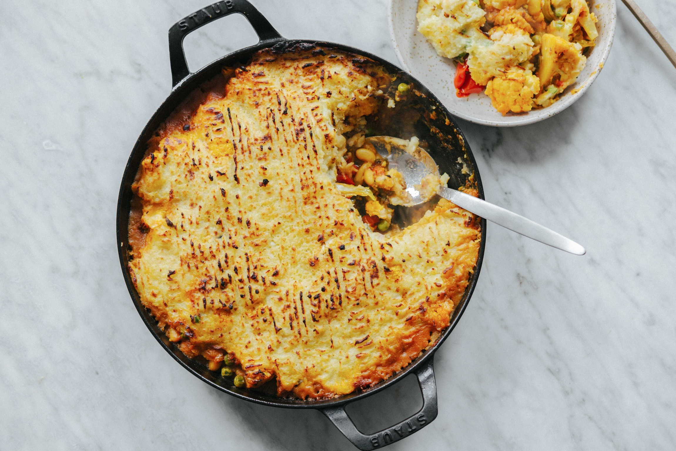 An aerial photo of a black dutch oven with a layer of brown potato, a spoon scooping out some veggies