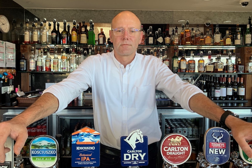 A man stands at the bar with a white shirt and glasses