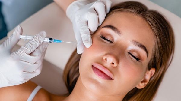 Young woman having injection inserted into cheek by hands wearing white plastic gloves.