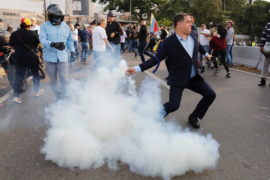 An opponent to Venezuela's President Nicolas Maduro returns a tear gas canister thrown from military personnel