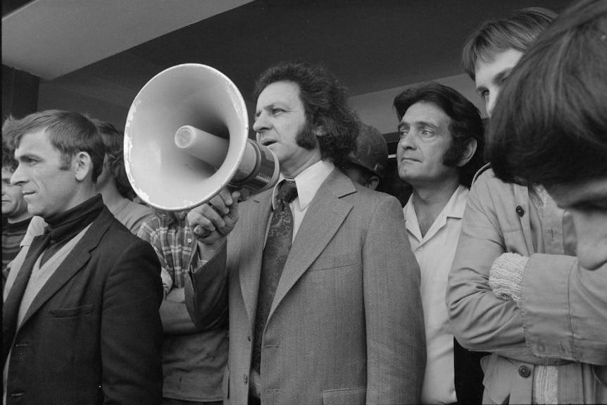 A black and white photo of a man in suit with a megaphone.