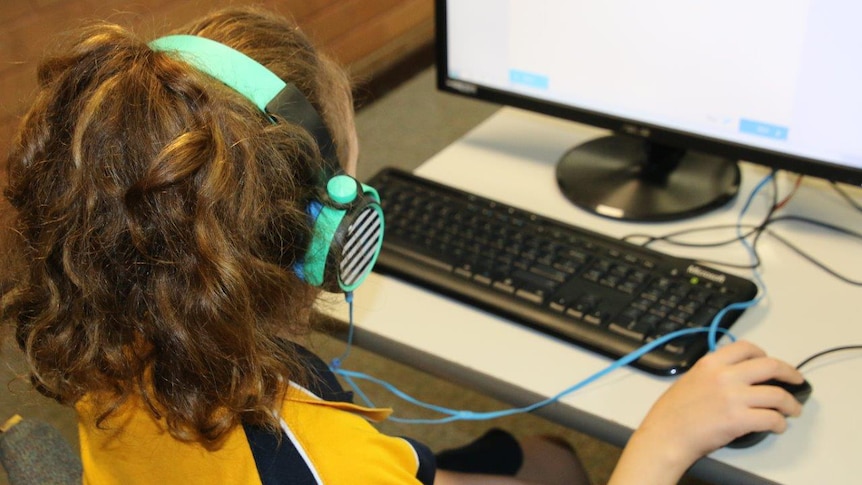 A primary school-aged girl wearing headphones works on a computer.
