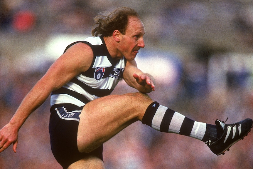 Gary Ablett Sr, seen from the side, kicks a football during an AFL game for the Geelong Cats.