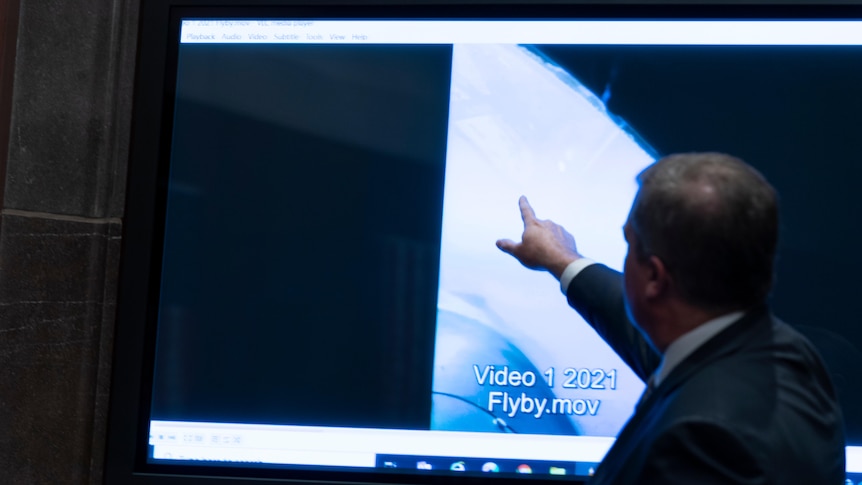 A man points at a TV screen showing footage of an unidentified flying onbject
