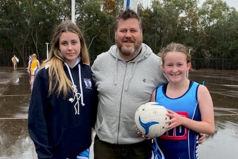 Ruby, Rodney and Poppy Templeton stand on a netball court for a photo.